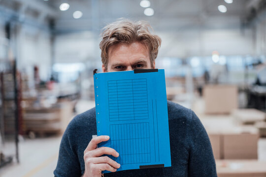 Businessman covering face with file in workshop