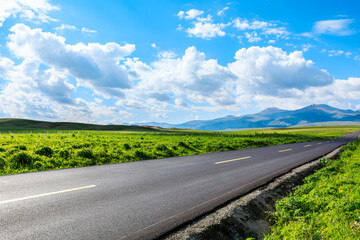 Country road and green meadow with mountain nature landscape under blue sky