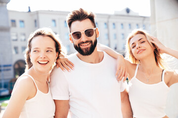 Group of young three stylish friends posing in the street. Fashion man and two cute female dressed in casual summer clothes. Smiling models having fun. Cheerful women and guy outdoors at sunny day