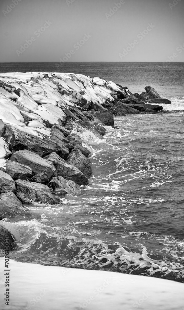 Wall mural Rocks above the sea covered in snow after a snowstorm. Weather and climate change concept