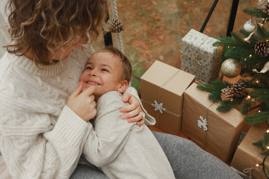 Loving mother embracing son near Christmas presents at home