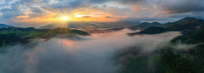 Amazing morning fog in the mountains. Beautiful sunrise light shines on the red beech forest. Drone panorama.