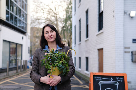Smiling mature woman standing with potted plant near buildings