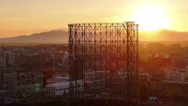 Alba sul Gazometro del quartiere post industriale Ostiense a Roma, Italia.
Veduta aerea con drone dei raggi del sole che passano attraverso la vecchia struttura del Gasometro.