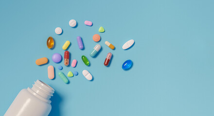 Top view of an open pill bottle and assorted medications scattered on blue colored background with...