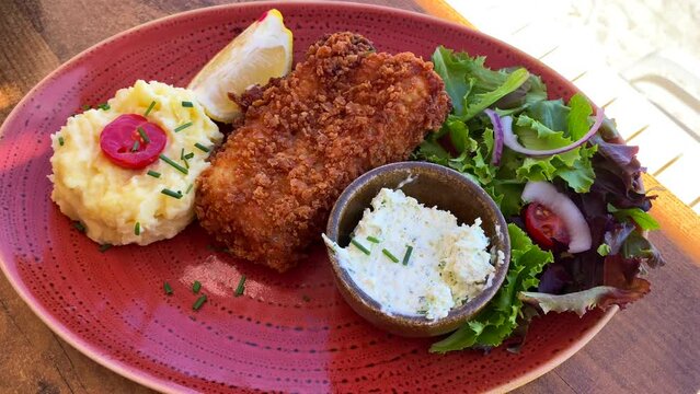 Delicious deep-fried fish with mashed potatoes and salad on a red plate, seafood, 4K shot