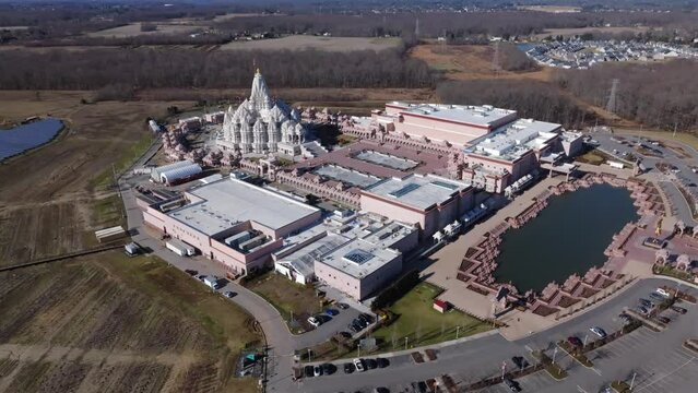 An aerial view of the Shri Swaminarayan Mandir in Robbinsville Township, NJ on a sunny day, it was closed for the day. The camera dolly out and tilt up from the massive temple.