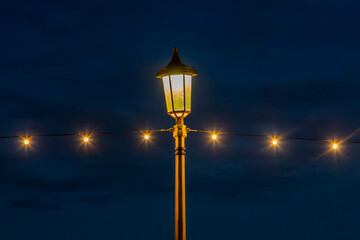 A night view at a coastal promenade with string lights and a lamp post