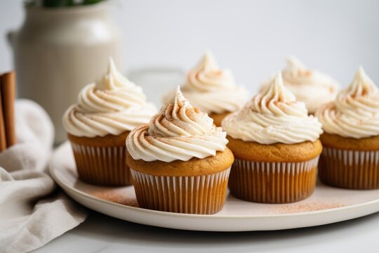  a plate of cupcakes with white frosting on top of a white plate next to a vase of flowers.