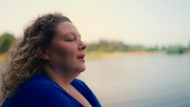 Inspired plump woman looking at river water and smiling, enjoying solitude