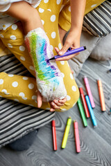 Teen girl with a broken arm at home draws an orthopedic cast