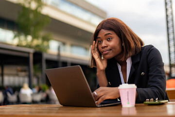 Seated in an urban setting, the businesswoman of color deals with a headache during her coffee break as she checks her agenda for the day.