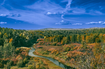 A winding river in the middle of an autumn forest with a blue sky with clouds.