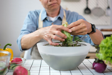 Senior man washing the vegetables from the garden while making healthy salad in kitchen.