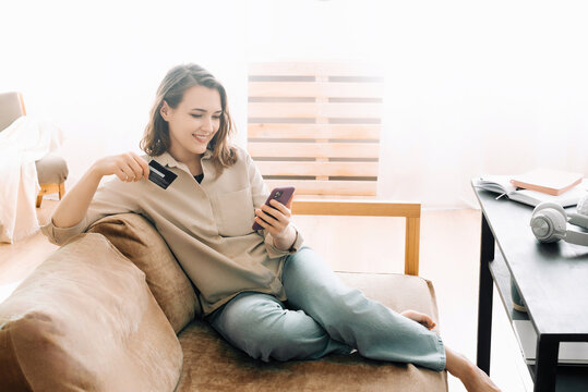 Remote Shopping Delight. Cheerful young woman with credit card types on smartphone, making online purchase. E-commerce, Mobile Payment, and Digital Shopping Concept