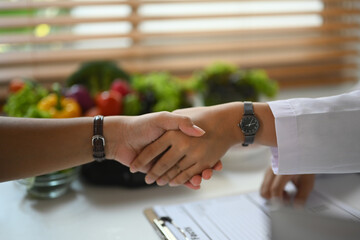 Cropped shot nutritionist shaking hands with patient at consultation in medical clinic. Health care...