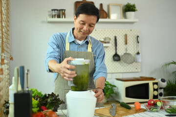 Happy middle aged man making vegetable smoothie with blender. Healthy eating lifestyle concept