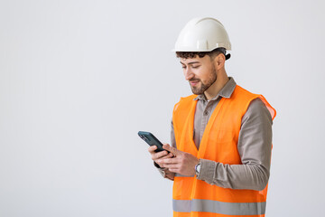 Young man worker or builder in yellow helmet and overall with smartphone over white background