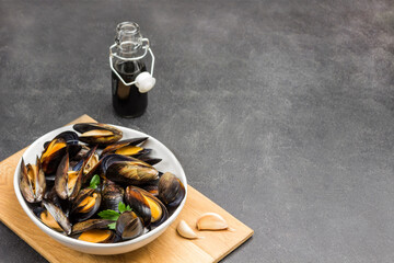 Mussels with open shells in white bowl on cutting board. Bottled water and sauce. Lemon and garlic