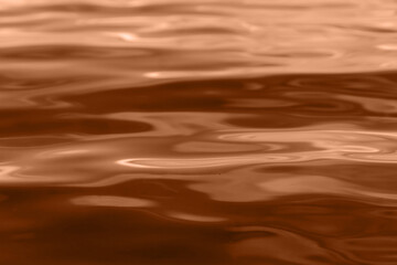Summer wave abstract or natural rippled water texture background toned in peach fuzz color. Intense dark river, lake or sea water texture. Trendy color of the year 2024. Design concept.