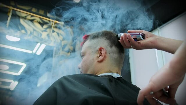 The hands of a hairdresser stylist cut a man's head with a clipper from behind, side view. Close-up. low angle shot