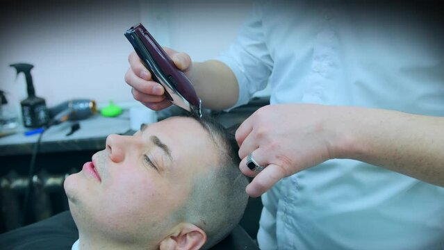 The hairdresser cuts the hair from the bangs of the client's head using a clipper. Side view. Close-up