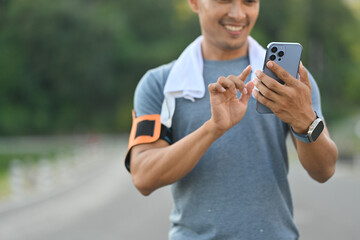 Satisfied athletic man using mobile phone resting after training outdoors