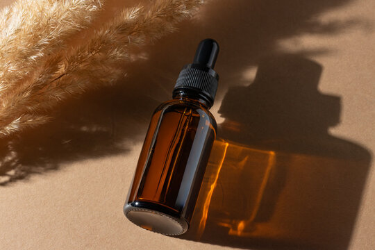 From above amber glass dropper bottle with a shadow on a beige background next to pampas grass