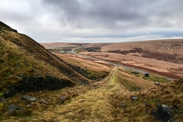 A grassy lane leads down to a main road cutting through the Yorkshire moors in West Yorkshire.