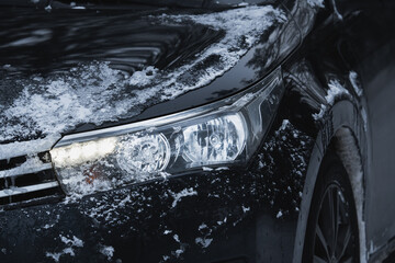 Car headlight with LED running lights.  Car with ice on the body, close-up photo.