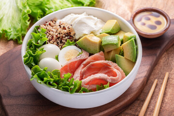 Salmon quinoa bowl with greens and vegetable on the wooden table. Balance in bowl. Top view.