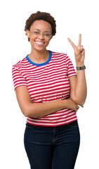 Beautiful young african american woman wearing glasses over isolated background smiling with happy face winking at the camera doing victory sign. Number two.