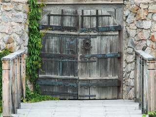 Old wooden gate with forged hinges in a stone wall