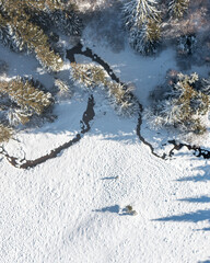 Aerial view of a small river, creek flowing amongst tree and snowy fields