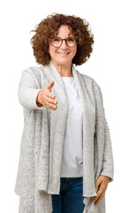 Beautiful middle ager senior woman wearing jacket and glasses over isolated background smiling friendly offering handshake as greeting and welcoming. Successful business.