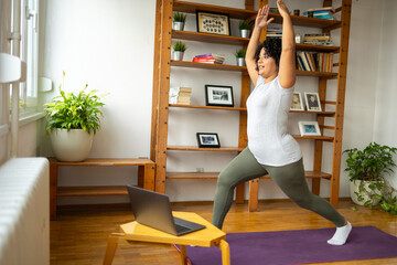 Woman practicing warrior pose during online classes in yoga room