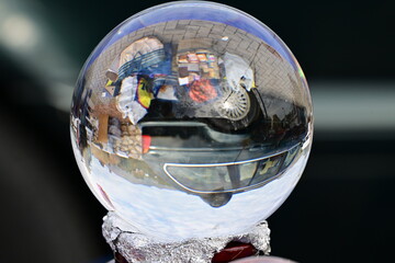 The reflection of a car and flea market stuff in a shiny glass sphere.