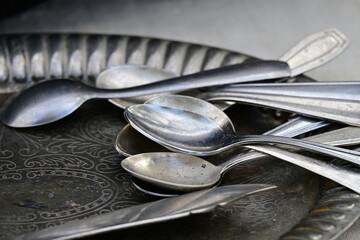Several old silver spoons on a shiny, antique tray.