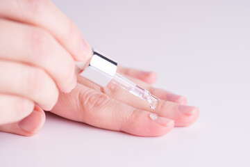 Pipette with a colorless drop of anti-brittle nails or oil for cuticles. The woman cares for hands...