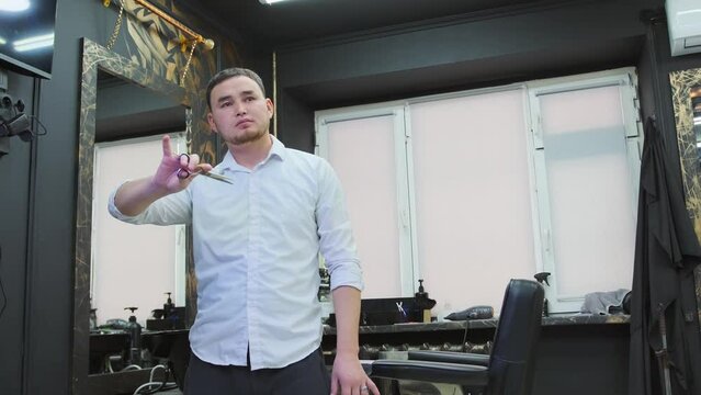 A hairdresser in a beauty salon is playing with scissors, pretending that he is cutting someone's hair, luring customers.