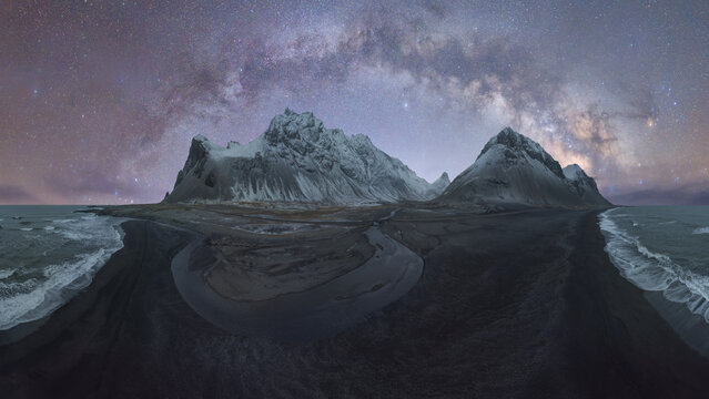 Panoramic view of a snow-covered mountain range with a foreground of winding rivers against the backdrop of the Milky Way in Iceland