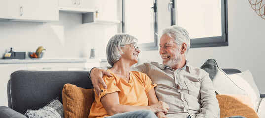 Happy laughing older married couple talking, laughing, standing in home interior together, hugging with love, enjoying close relationships, trust, support, care, feeling joy, tenderness. - Powered by Adobe