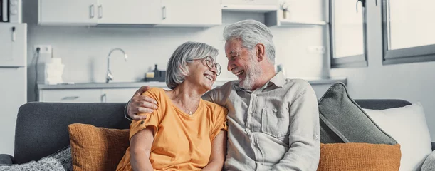 Fotobehang Happy mature husband and wife sit rest on couch at home hugging and cuddling, show care affection, smiling senior loving couple relax on sofa have fun, enjoy tender romantic family weekend together. © Daniel