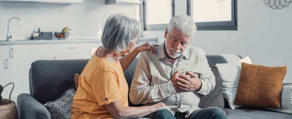 Grey haired man touching chest, having heart attack, feeling pain, suffering from heartache disease at home, mature woman supporting, embracing him, middle aged family, horizontal banner, close up.