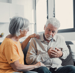 Grey haired man touching chest, having heart attack, feeling pain, suffering from heartache disease at home, mature woman supporting, embracing him, middle aged family, horizontal banner, close up.