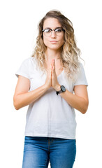 Beautiful young blonde woman wearing glasses over isolated background praying with hands together asking for forgiveness smiling confident.