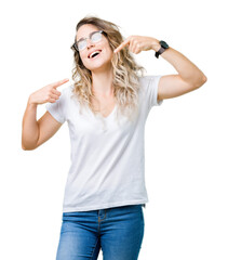 Beautiful young blonde woman wearing glasses over isolated background smiling confident showing and pointing with fingers teeth and mouth. Health concept.