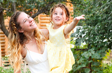 Beautiful happy family of mother and little daughter under summer rain in green garden