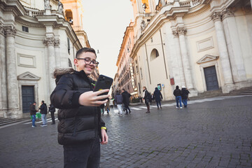 Smiling Happy tourist  boy with   eyeglasses  enjoy the city of Rome ,taking photos with a phone  at during language vacation.Concept  family travel trip happy language vacations in Rome