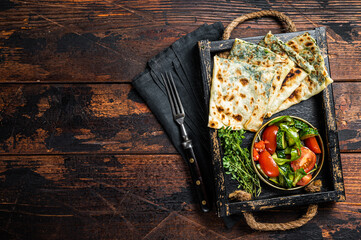 Baked Gozleme flatbread with greens in a box with vegetable salad. Wooden background. Top view. Copy space - obrazy, fototapety, plakaty